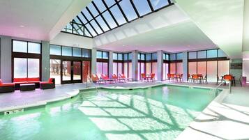 An indoor swimming pool with clear glass ceilings, sunlit areas with lounge chairs, and a visible lifeguard station.