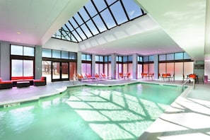 An indoor swimming pool with clear glass ceilings, sunlit areas with lounge chairs, and a visible lifeguard station. - Hilton Mystic (Mystic)