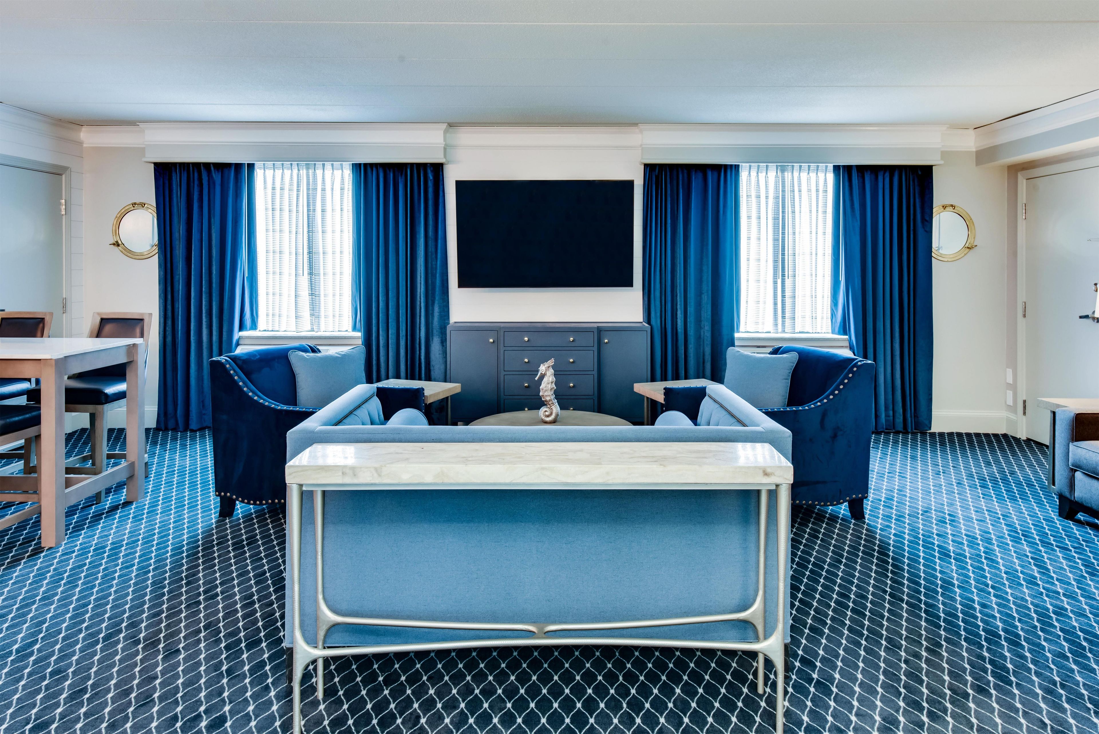A hotel room with a large bed, two armchairs, a small table, a TV, and a minibar.