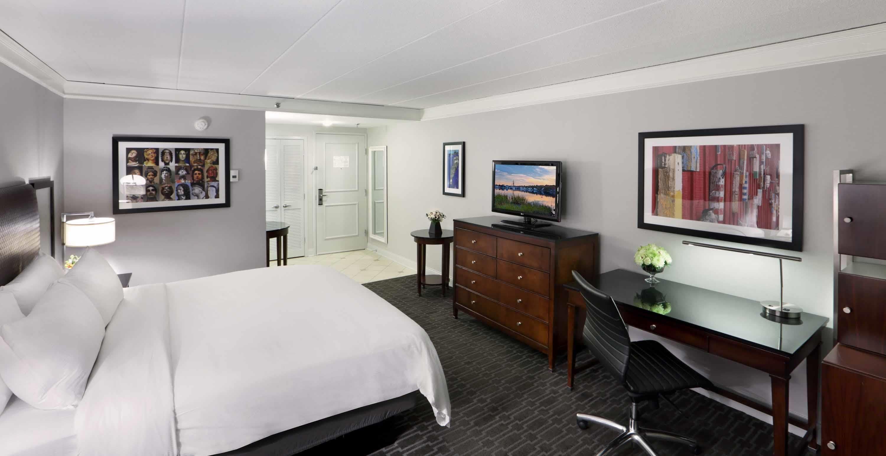 A hotel room with a bed, a desk, a television, a dresser, and a framed picture on the wall.