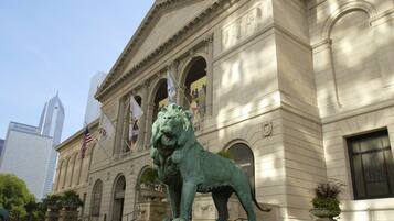 A neoclassical building with a lion statue in front, flags, and a clear sky.