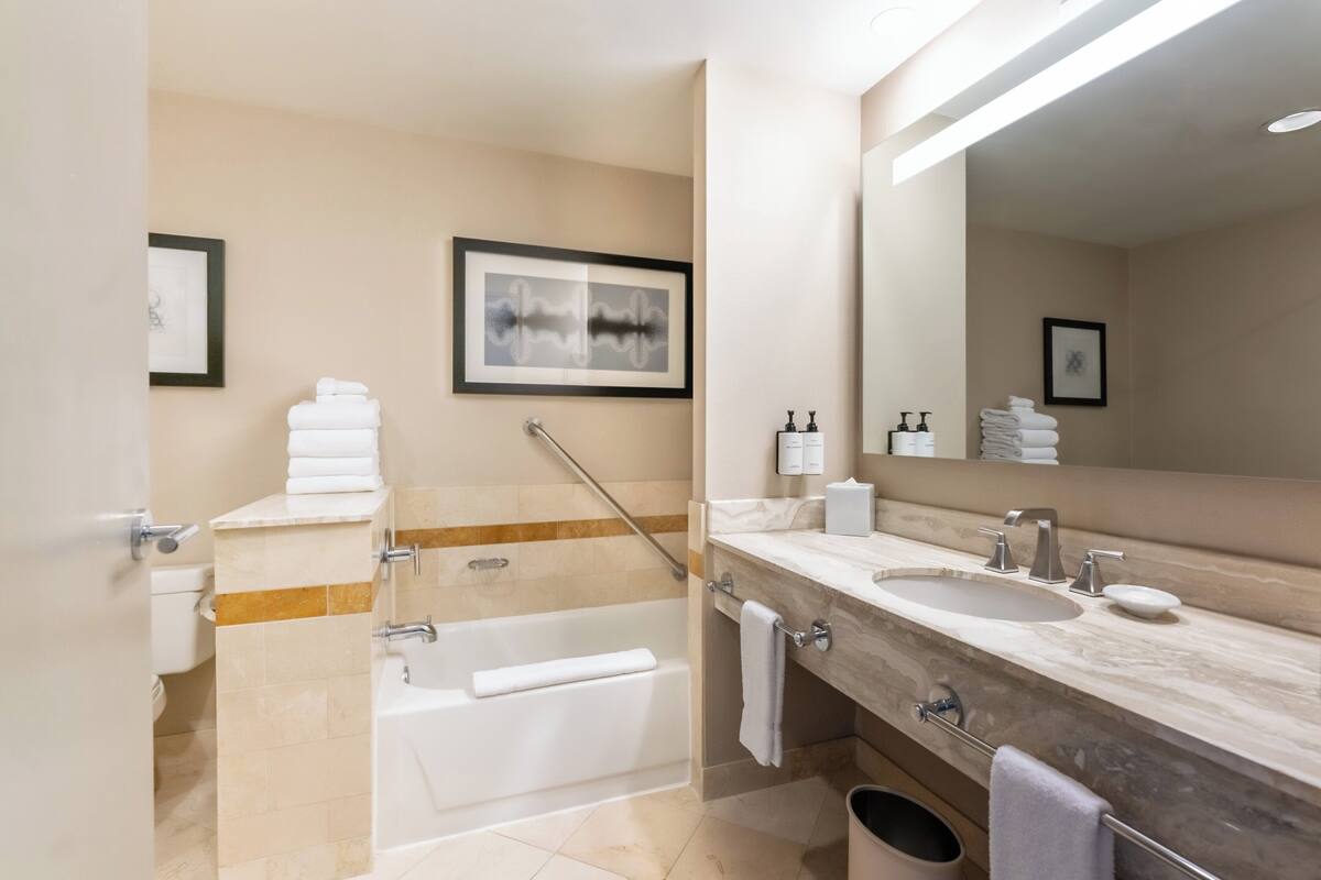Un baño moderno con bañera, un espejo grande y un tocador con lavamanos y toallero.