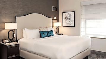 Habitación de hotel con una cama grande, dos mesitas de noche con lámparas, una obra de arte en la pared y una ventana con persianas.