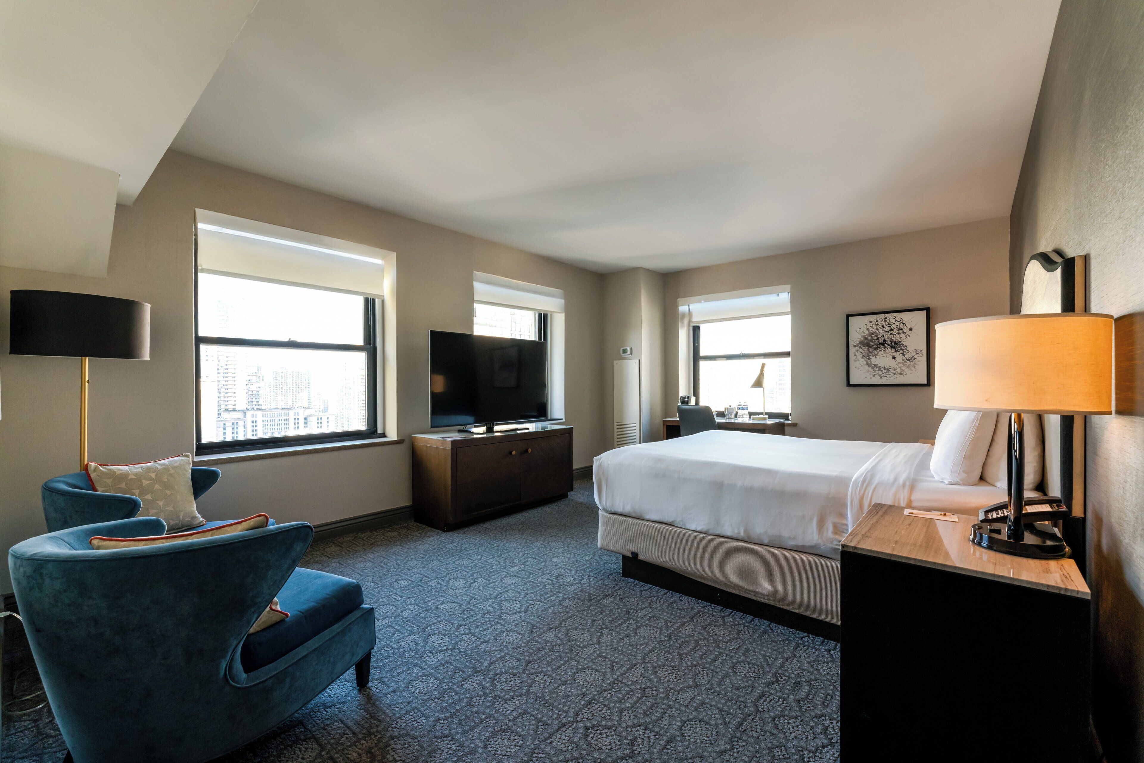 A hotel room with a large bed, a desk, a TV, and a chair.