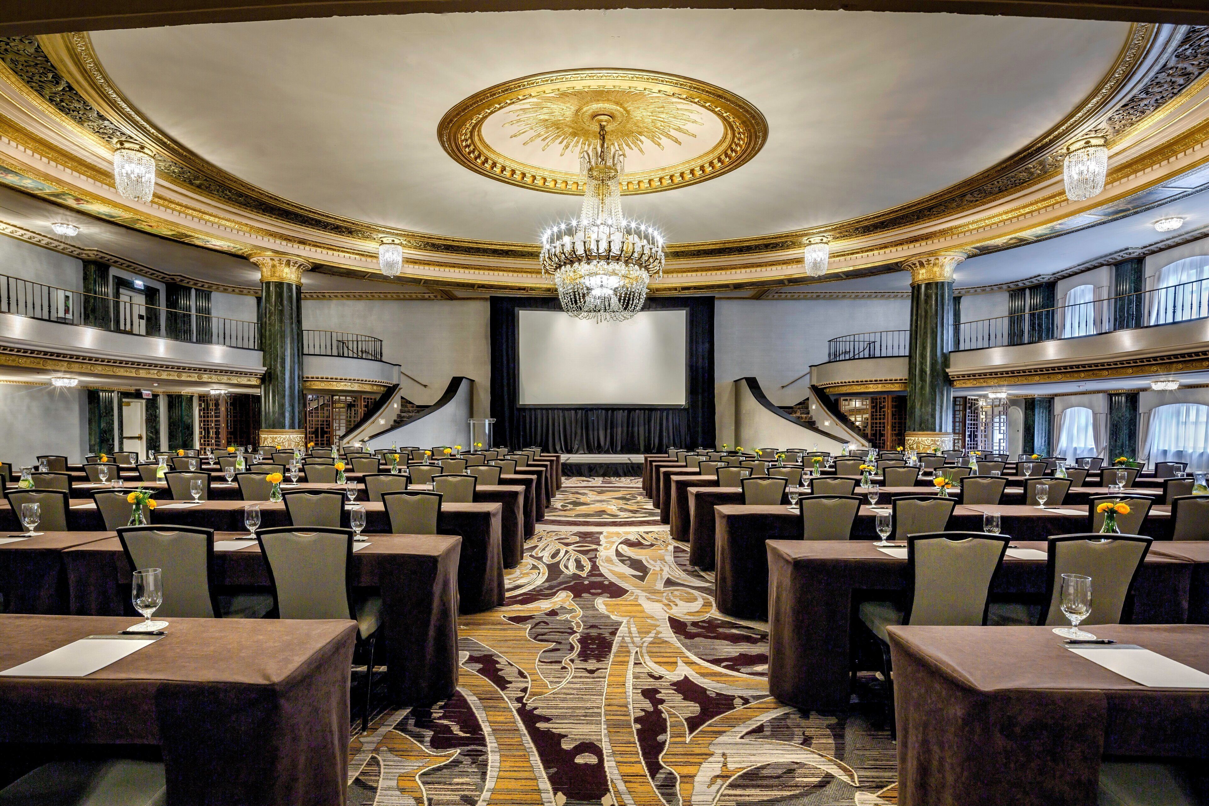 A grand ballroom with a central stage, ornate ceiling, and multiple seating arrangements.