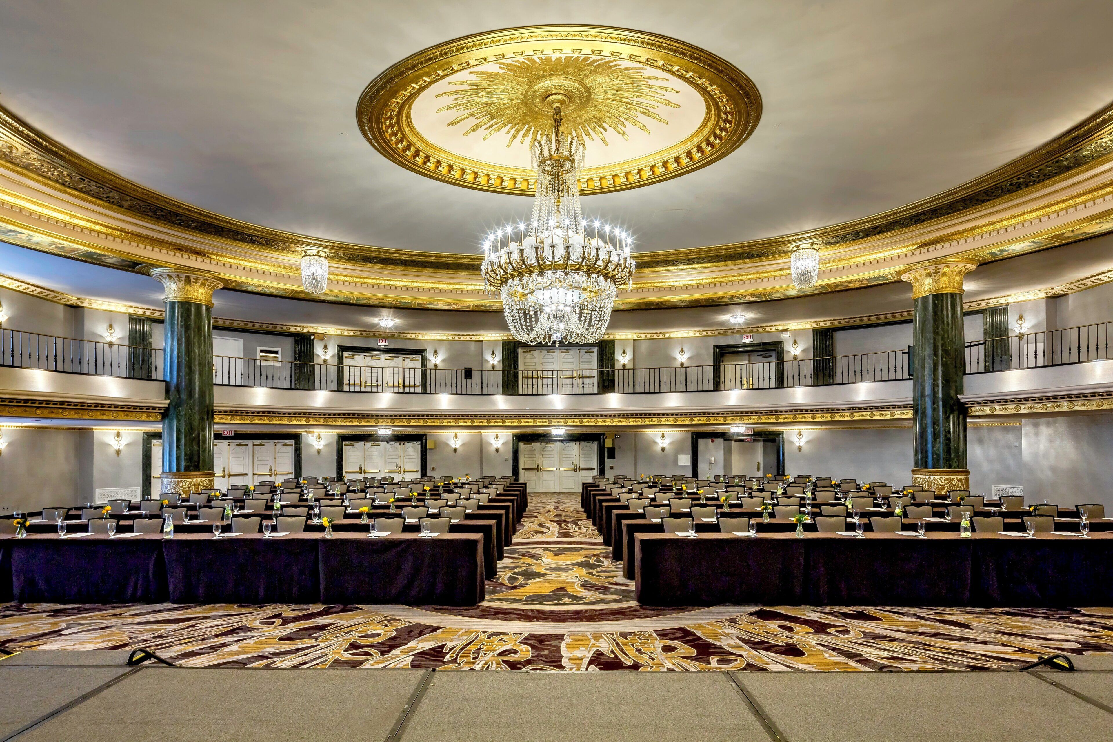 A grand hall with a large chandelier, multiple levels, and rows of tables set for meetings.