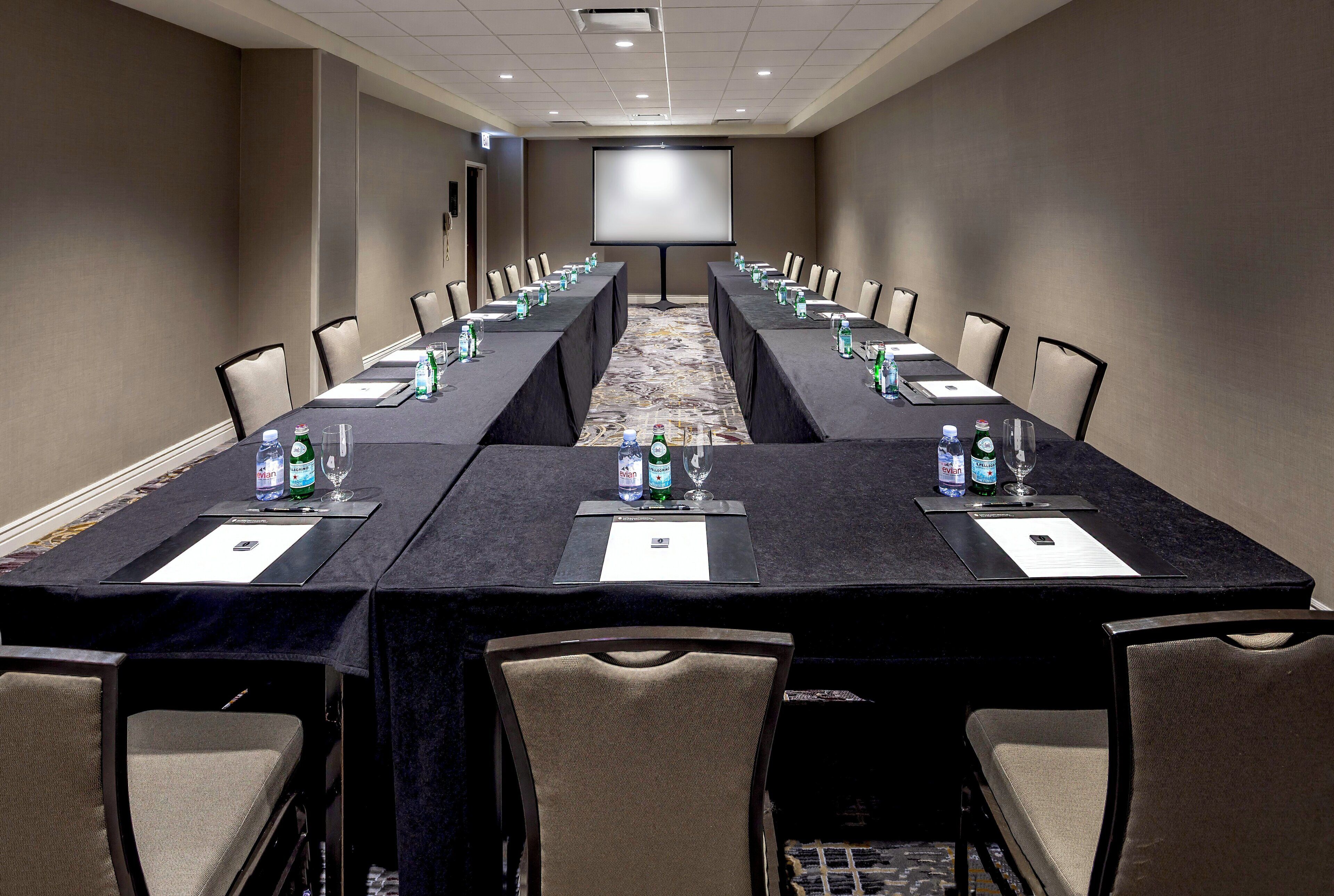 A conference room with a long table, chairs, water bottles, and a projector screen.