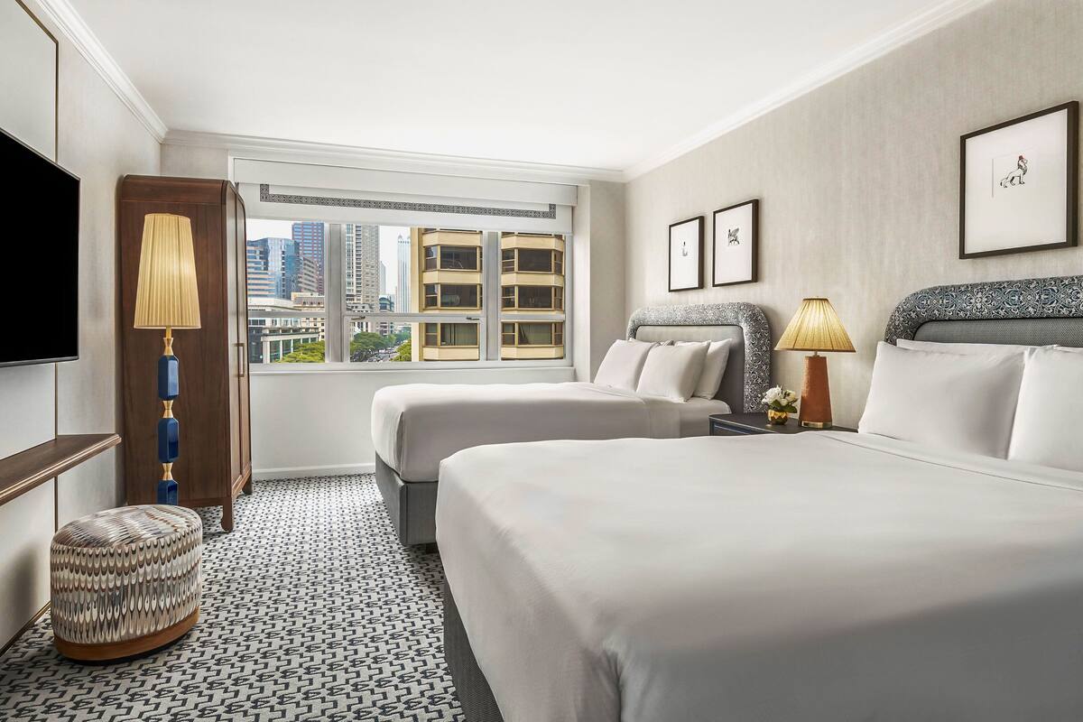 Habitación de hotel con dos camas, televisión, ventana con vista a la ciudad y suelo estampado.