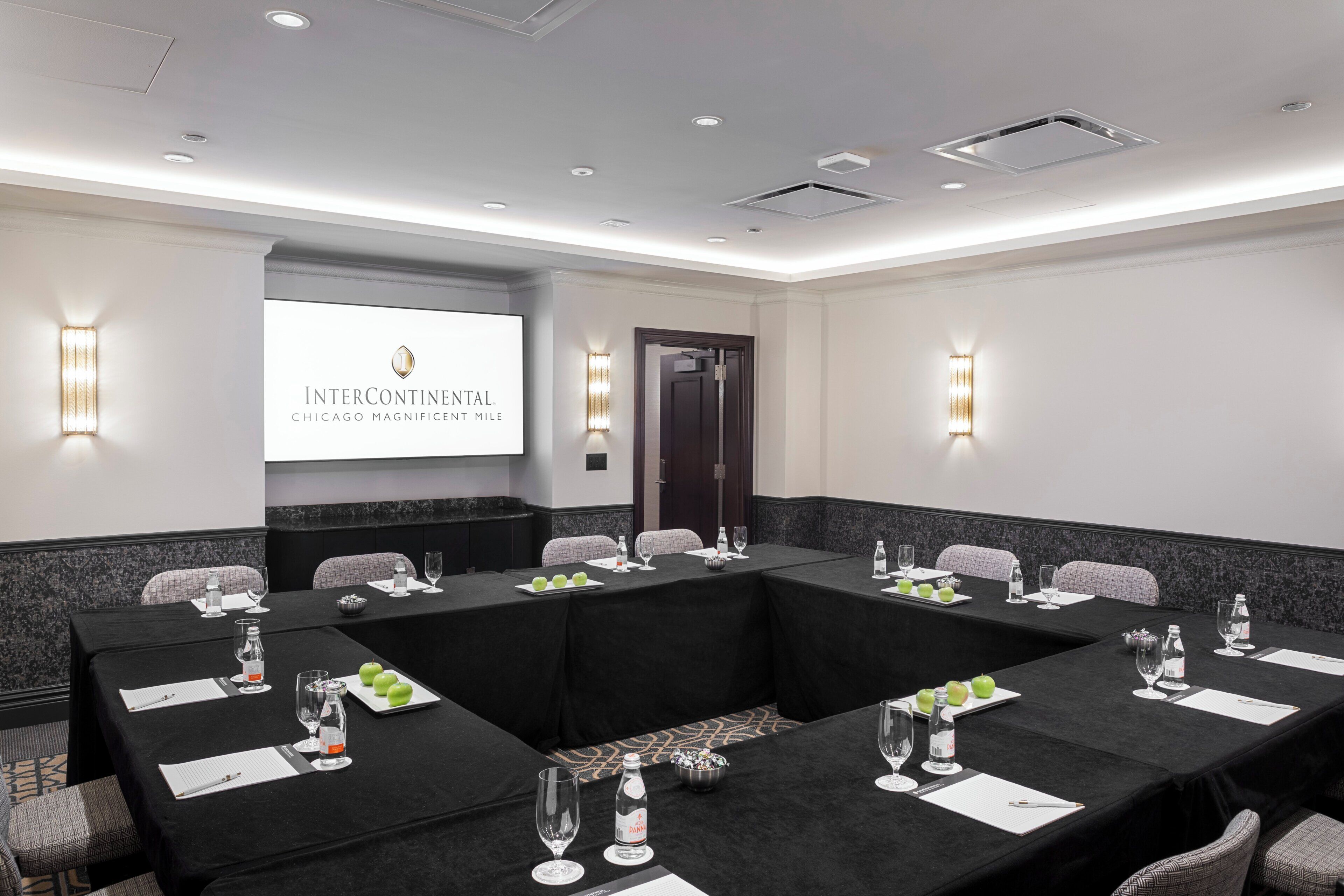 A conference room with a long table, chairs, and a projector screen displaying 'InterContinental Chicago Magnificent Mile'.