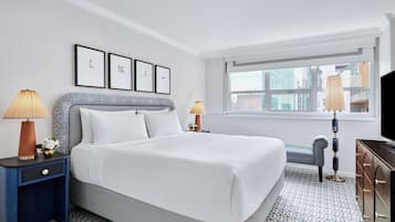 A hotel room with a large bed, two bedside tables, a dresser, a window with a view of buildings, and framed pictures on the wall.