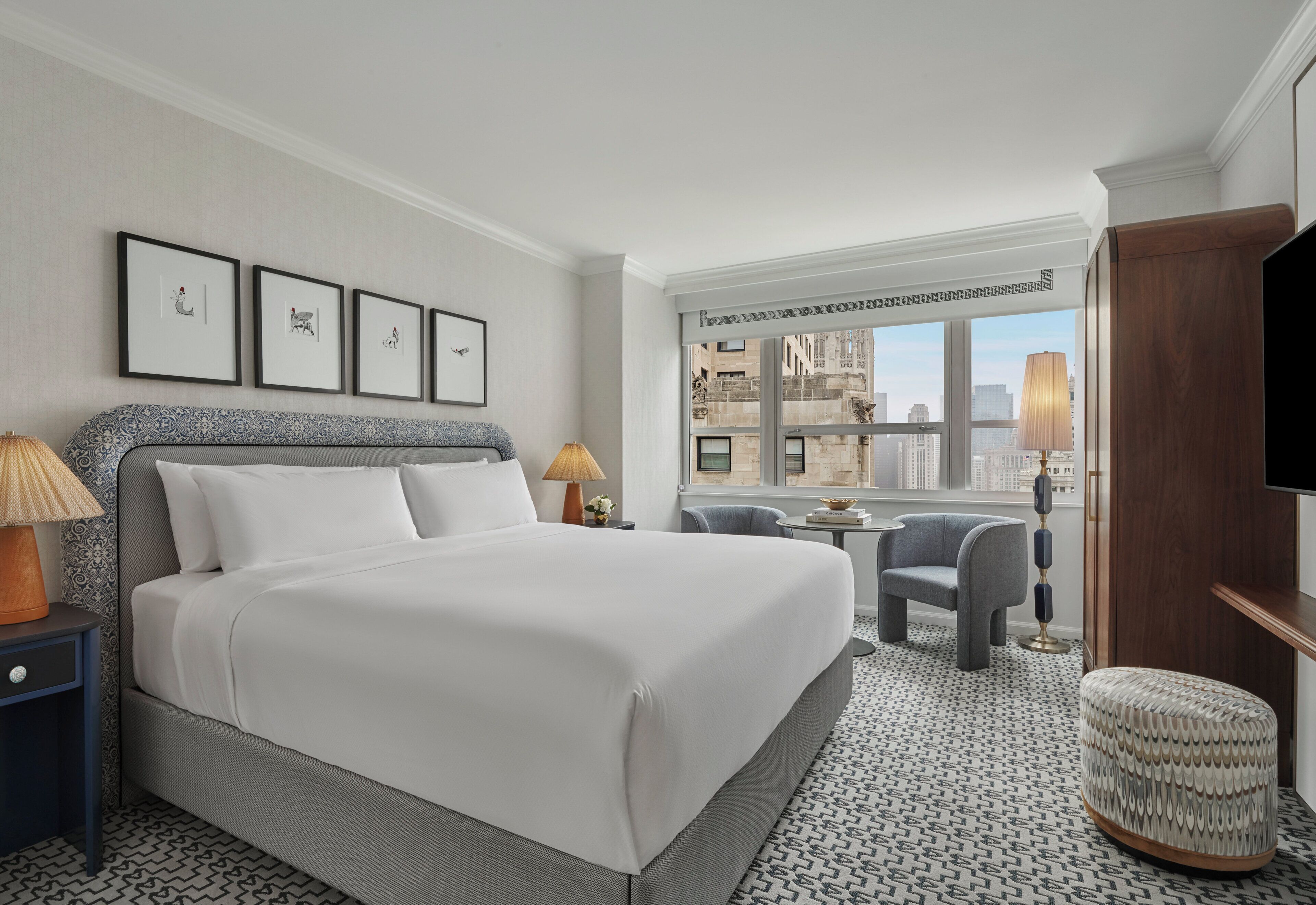 Quarto de hotel com uma cama grande, uma escrivaninha, uma cadeira e uma televisão.