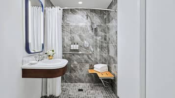 Un baño moderno con ducha de mármol, lavamanos con espejo y un pequeño estante de madera con toallas.