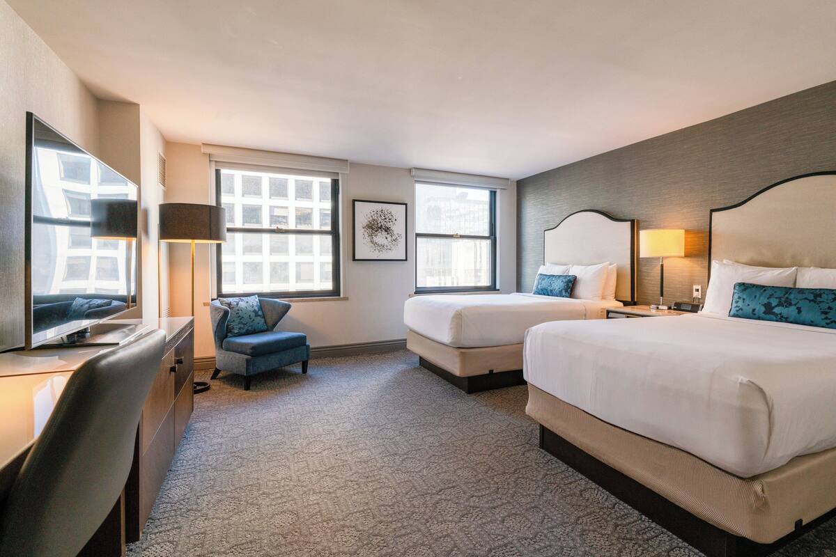 Una habitación de hotel con dos camas, un escritorio, una silla y un ventanal grande.