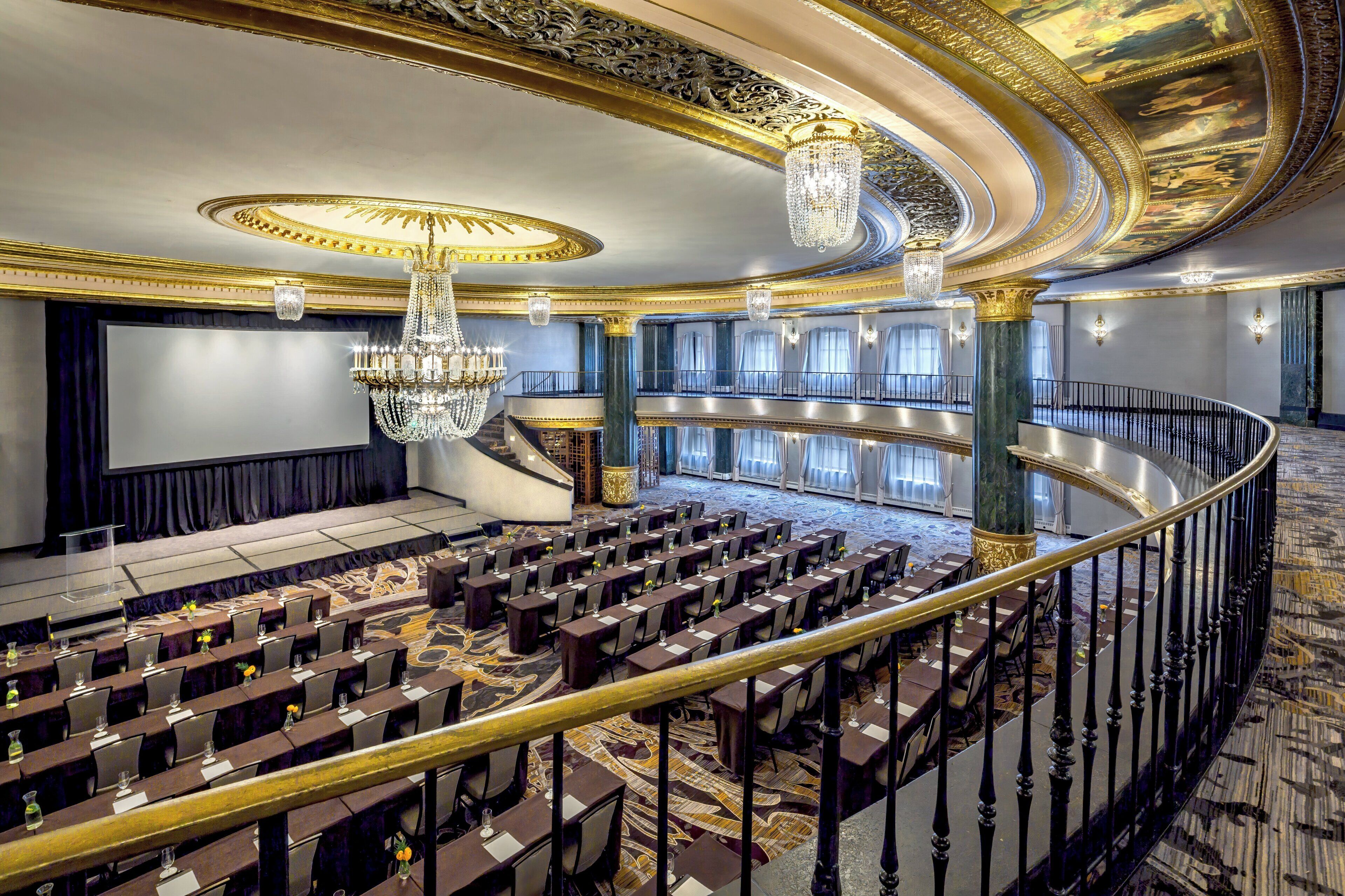 A grand hall with tiered seating, ornate chandeliers, and a marble floor.