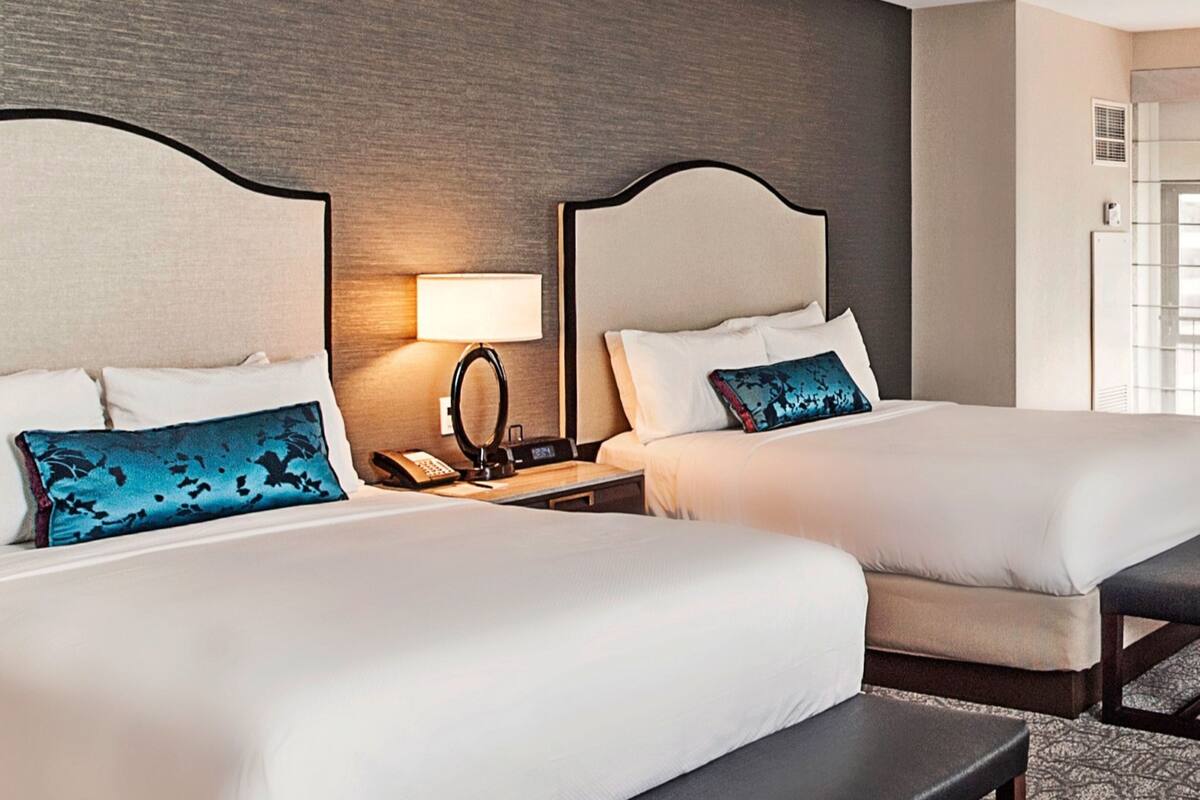 Una habitación de hotel con dos camas, una mesita de noche con lámpara y una pequeña mesa.