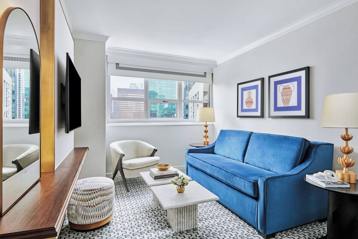 Una sala de estar moderna con un sofá azul, un sillón blanco, una mesa de centro y un televisor montado en la pared.