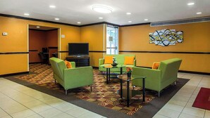 Un hall de hotel con sofás verdes, un televisor, una alfombra estampada y un cuadro abstracto grande en la pared.
