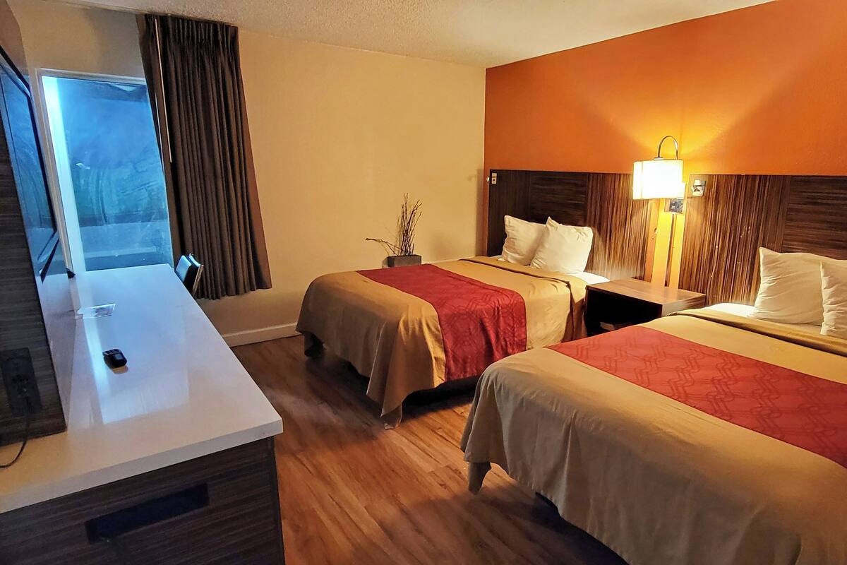 Ein Hotelzimmer mit zwei Betten, einem Schreibtisch, einem Fernseher und einem fensterbepflanzten Fenster.
