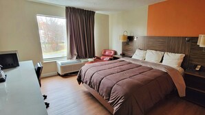 Habitación de hotel con cama, escritorio, silla, ventana con cortinas y una lámpara de pared.