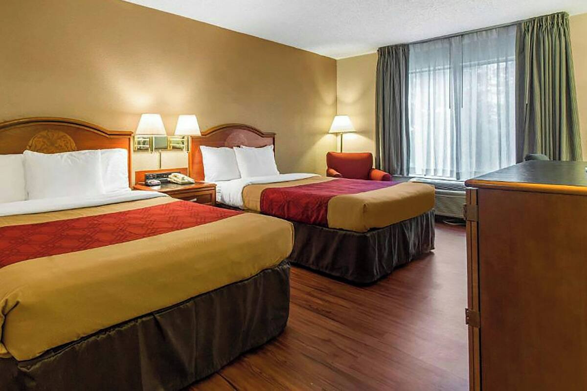 Ein Hotelzimmer mit zwei Betten, einem Schreibtisch, einem Stuhl und einem Fenster mit Vorhängen.