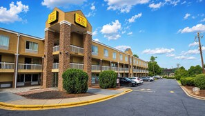 A hotel with a central tower, multiple balconies, and a parking lot. - Studios & Suites 4 Less Charlotte (Charlotte)