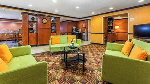 Un hall de hotel con sofás verdes, una estación de café, un televisor y un reloj en la pared.