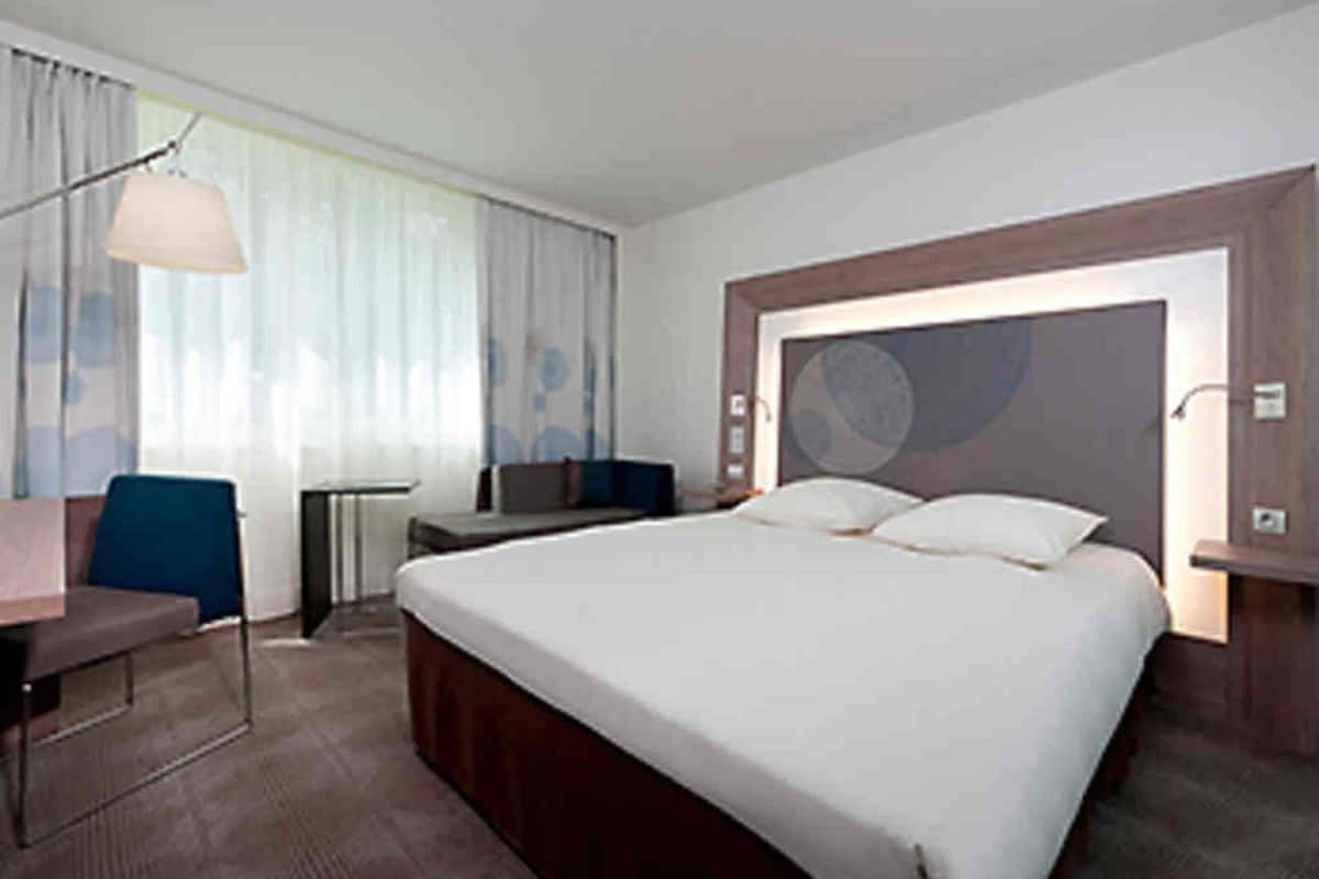 A hotel room with a large bed, a desk, a chair, and a lamp.