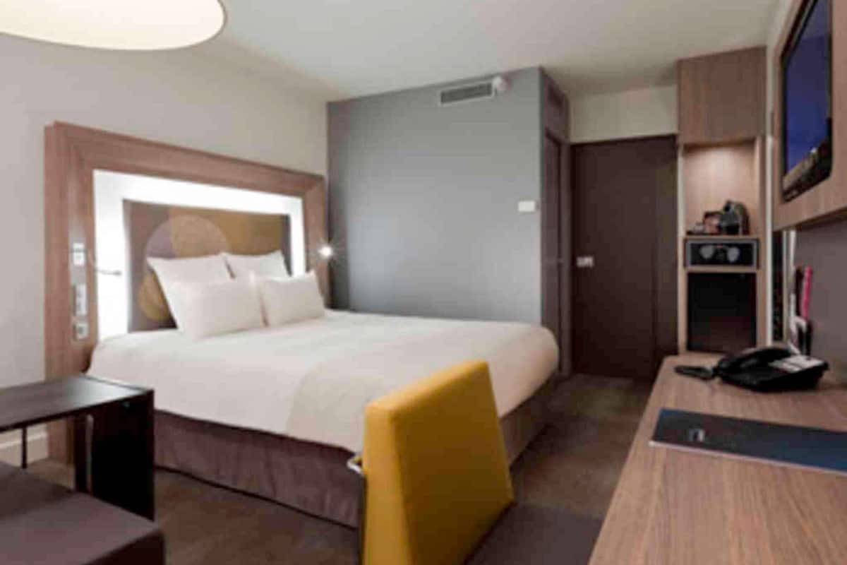 A hotel room with a bed, a desk, a chair, a television, and a wardrobe.