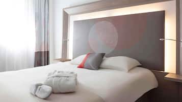 A hotel room with a large bed, a headboard with a geometric design, a bedside table, and a window with curtains.
