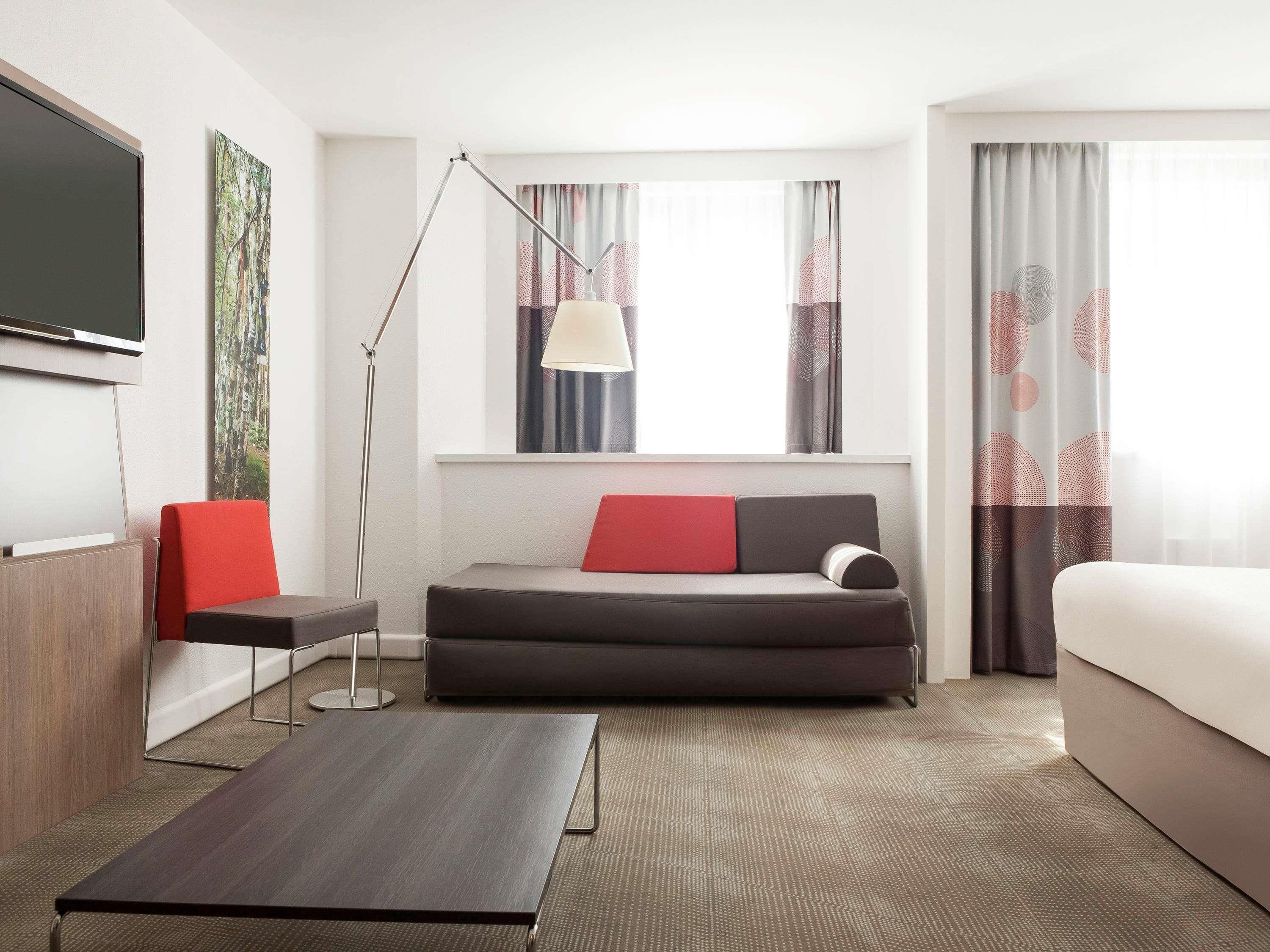 Une chambre d’hôtel moderne équipée d’un canapé, d’un lit, d’un bureau, d’une lampe sur pied et d’un téléviseur.