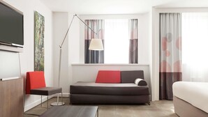 Una habitación de hotel moderna con sofá, cama, escritorio, lámpara de pie y televisión.