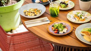 A dining table with plates of food, a green drink, and a wicker chair. - Novotel Paris Pont De Sevres (Sevres)