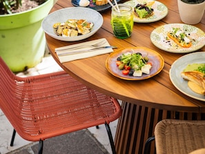 Une table à manger avec des assiettes remplies de nourriture, une boisson verte et une chaise en osier.