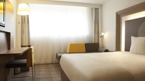 Una habitación de hotel con una cama, un escritorio, una silla, una lámpara y una ventana con cortinas.