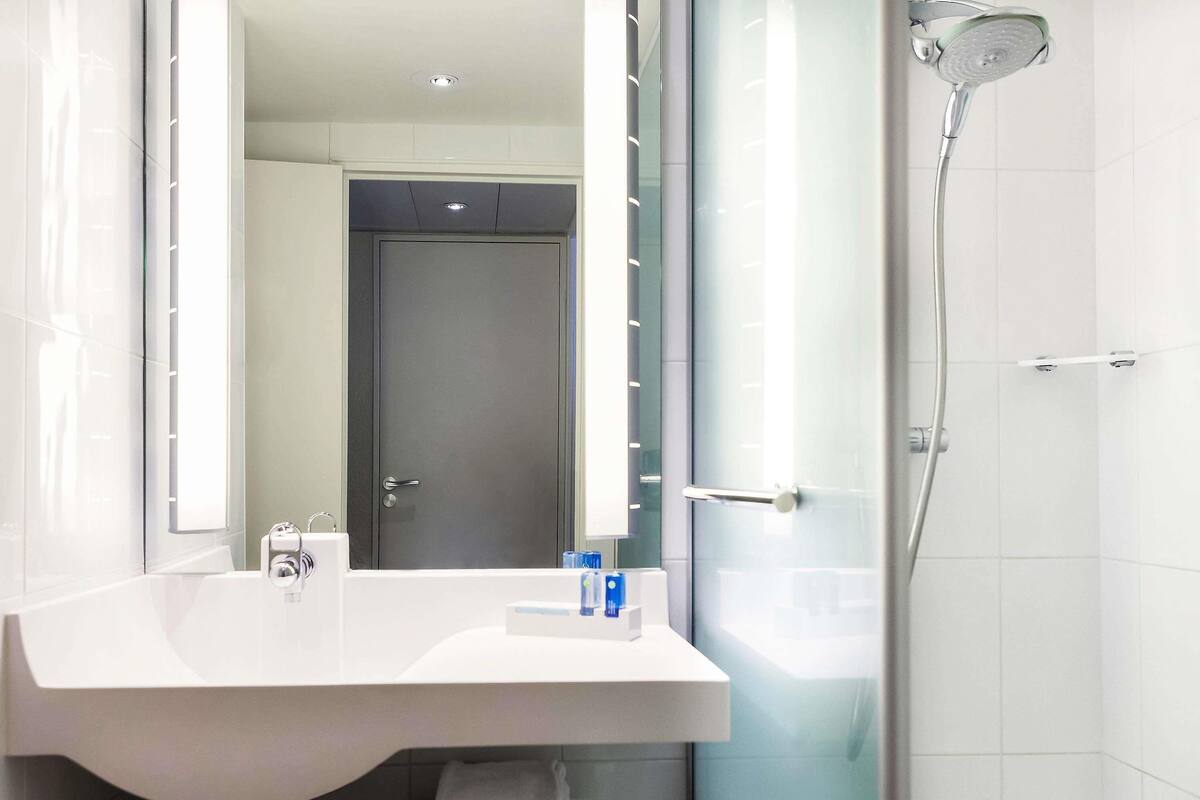 Een moderne badkamer met een grote spiegel, een douche en een wastafel met een handdoekhouder.