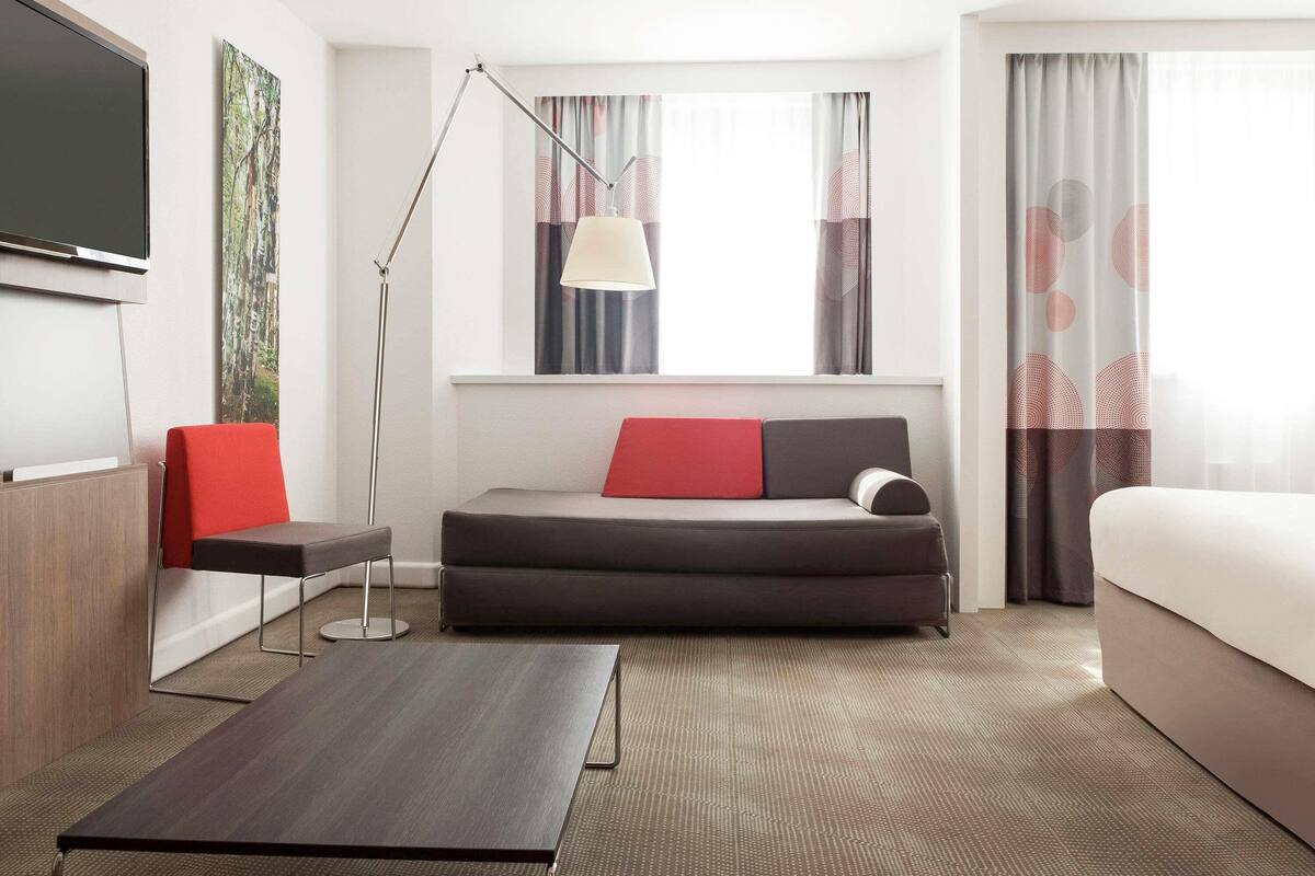 Een moderne hotelkamer met een bank, een bed, een bureau, een vloerlamp en een televisie.