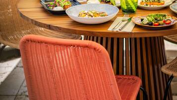 A round wooden table with various dishes, a glass of green drink, and a wicker chair.