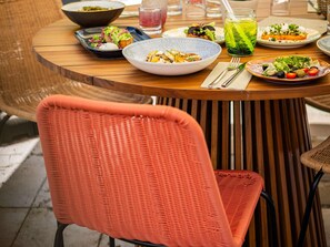 A round wooden table with various dishes, a glass of green drink, and a wicker chair.