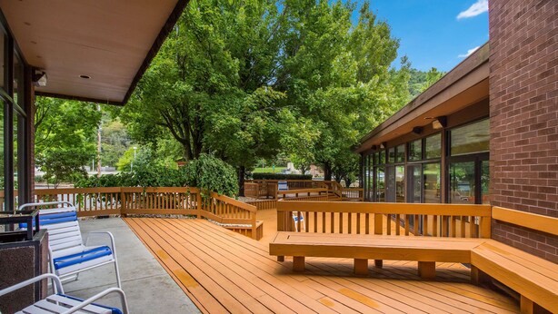 A wooden deck with benches and chairs, surrounded by trees and a brick building. - Best Western Braddock Inn (Cumberland)
