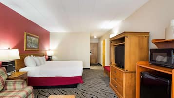 Een hotelkamer met een bed, een televisie, een koelkast, een houten kast, een bureau, een stoel en een schilderij aan de muur.