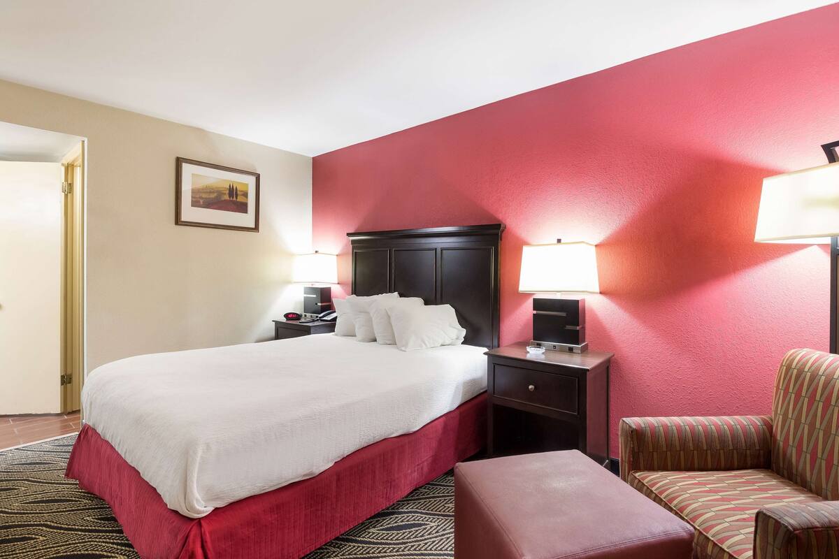 Quarto de hotel com cama grande, mesa de cabeceira, poltrona e escrivaninha com abajur.