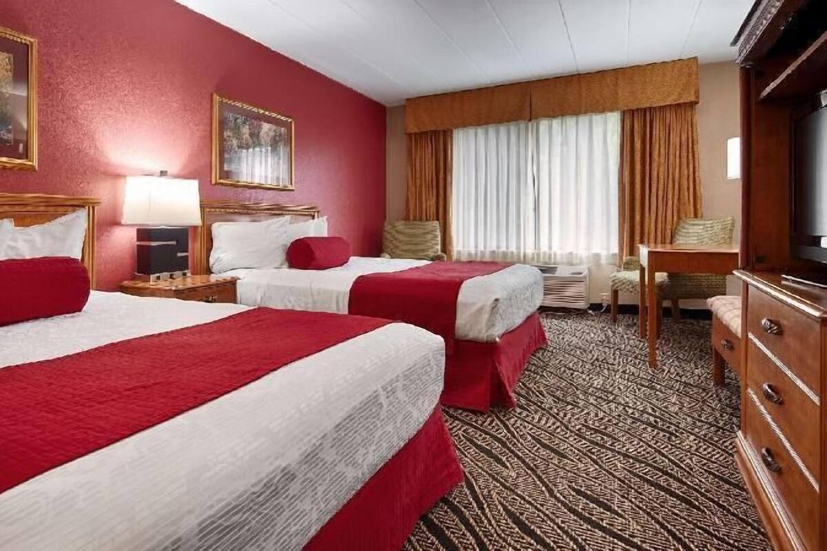 Quarto de hotel com duas camas, televisão, escrivaninha e janela com cortinas.