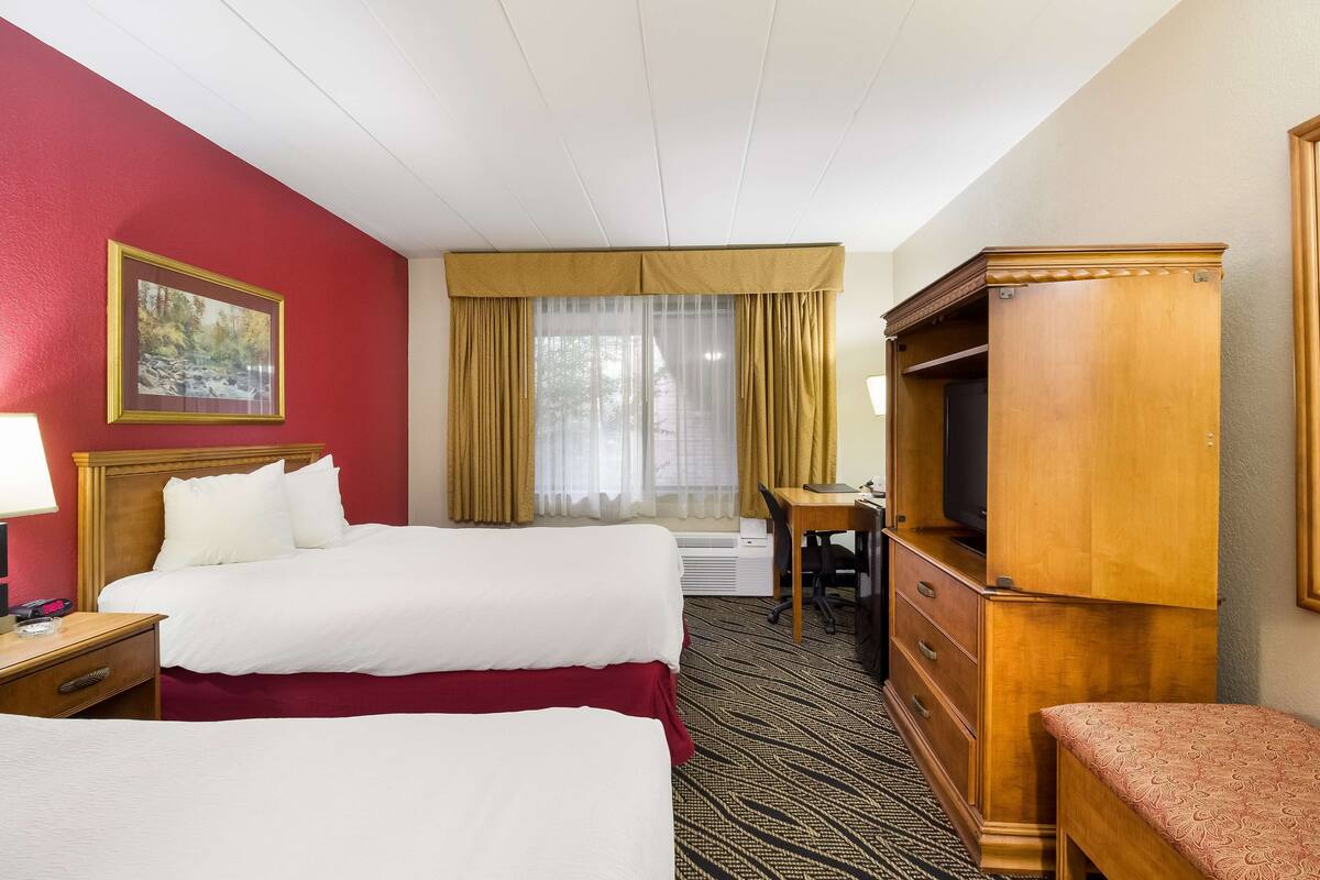 Quarto de hotel com duas camas, uma escrivaninha, televisão e janela com cortinas.