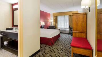 A hotel room with a bed, a desk, a chair, a mirror, a wardrobe, and a bathroom with a toilet and sink.