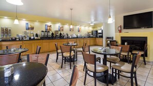 A modern kitchen with wooden cabinets, a central island, and a flat-screen TV mounted on the wall. - Best Western Braddock Inn (Cumberland)