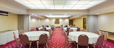 A conference room with multiple round tables, chairs, and a red carpeted floor.