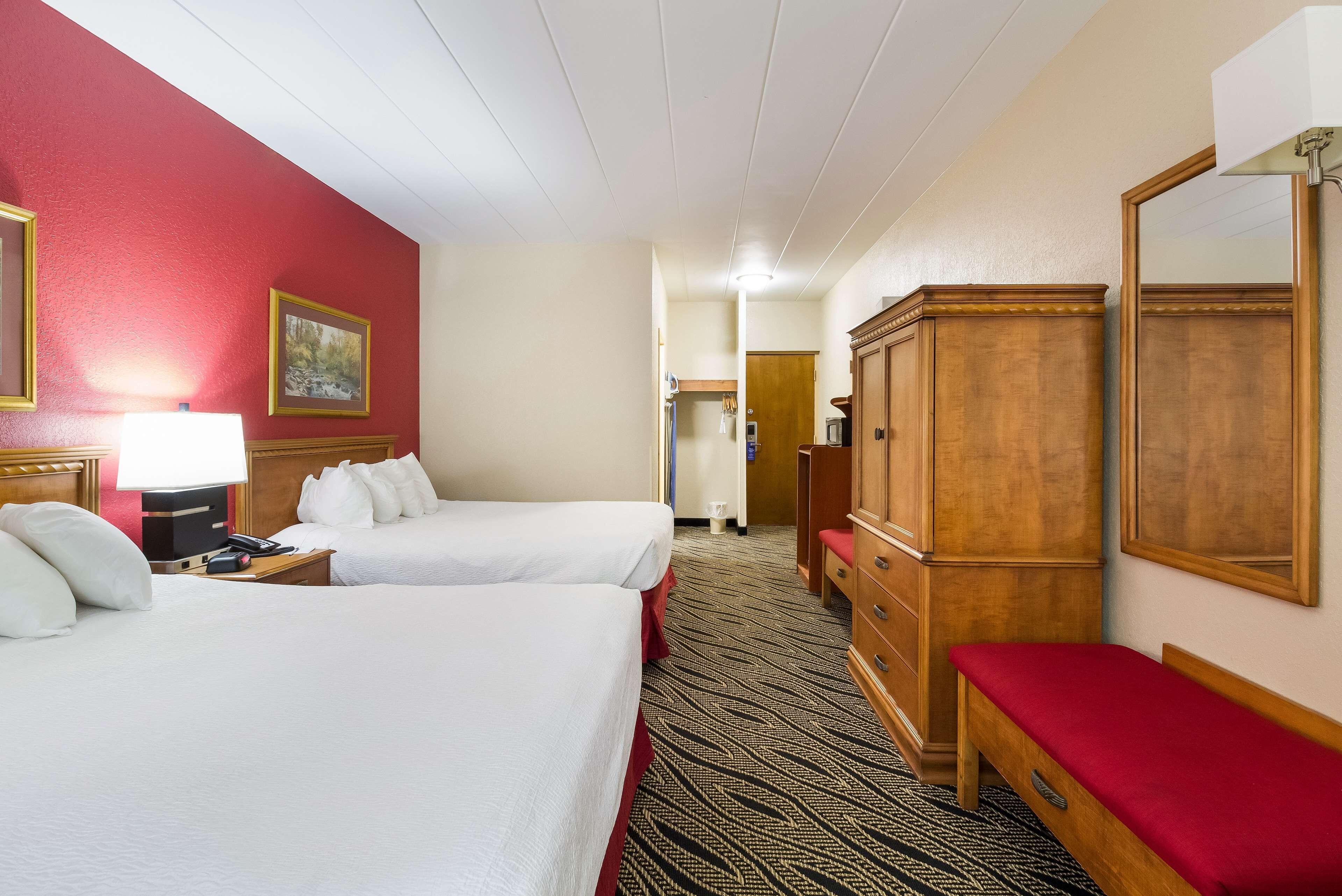 Une chambre d’hôtel avec deux lits, une commode en bois, un banc, une lampe et un tableau au mur.