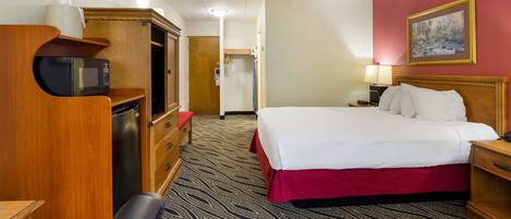 Une chambre d’hôtel avec un lit, un bureau doté d’un micro-ondes, un réfrigérateur, une armoire en bois, une moquette rouge et un tableau accroché au mur.
