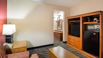 Une chambre d’hôtel avec un bureau en bois, un téléphone, une télévision, un réfrigérateur et un canapé à motifs.