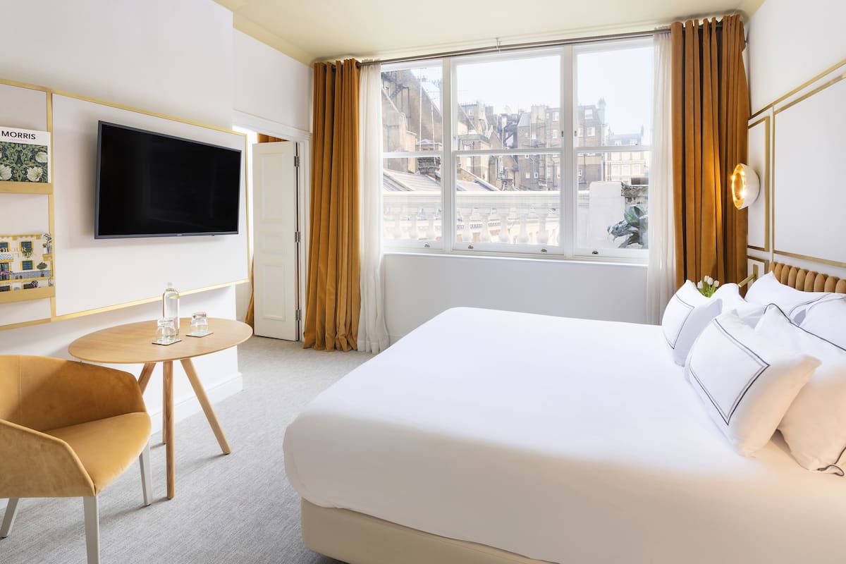 Ein Hotelzimmer mit einem großen Bett, einem an der Wand befestigten Fernseher, einem kleinen runden Tisch und einem Stuhl.